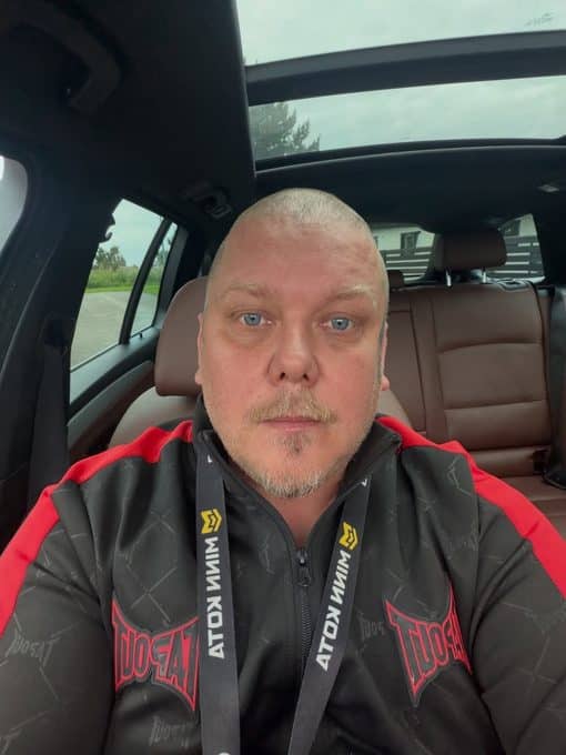 Pottukoira ottaa selfien auton sisällä musta-punaisessa takissa.